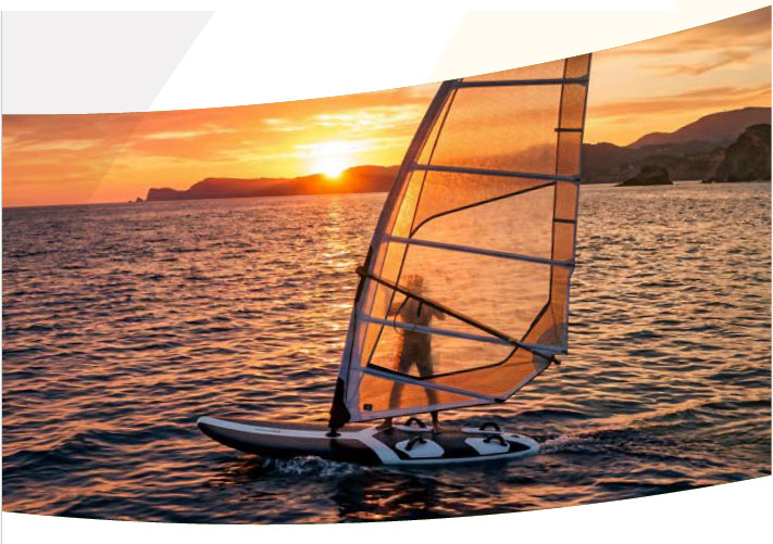 Mindeful Longevity Eine Person beim Windsurfen auf dem Meer im warmen Licht der untergehenden Sonne, mit einer bergigen Küste im Hintergrund.
